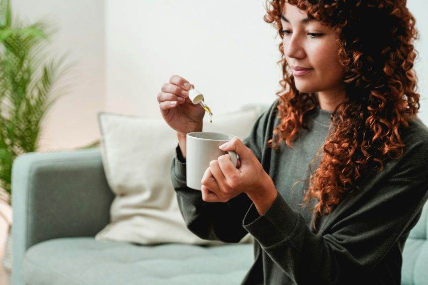 Cbd oil dropper - Young woman taking cannabis oil in tea drink for anxiety and stress treatment