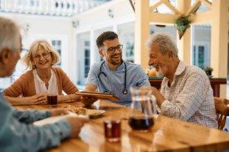 Happy healthcare worker and group of seniors having fun on patio at nursing home.