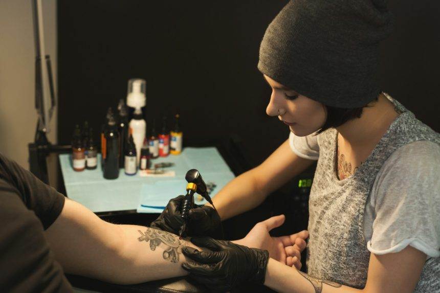 Young woman tattooist doing tattoo on male arm